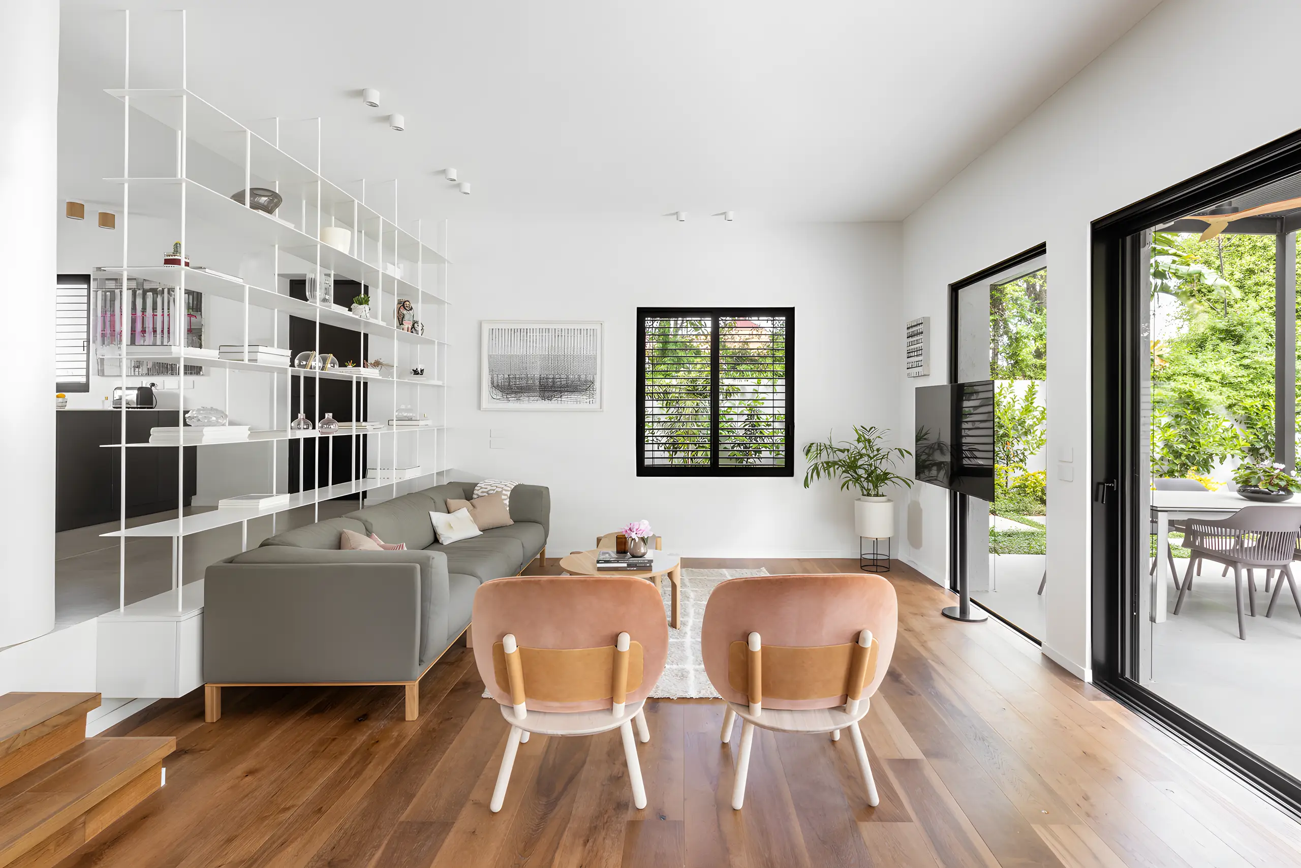 White shelving wall, leather armchairs and a grey sofa with the garden through the glazing