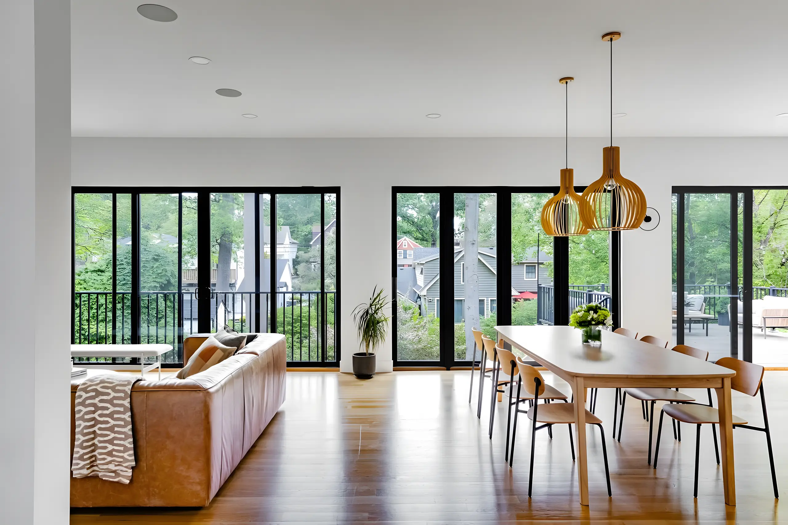 Open living and dining room with natural oak floors, black-framed glazing and a tan leather sofa