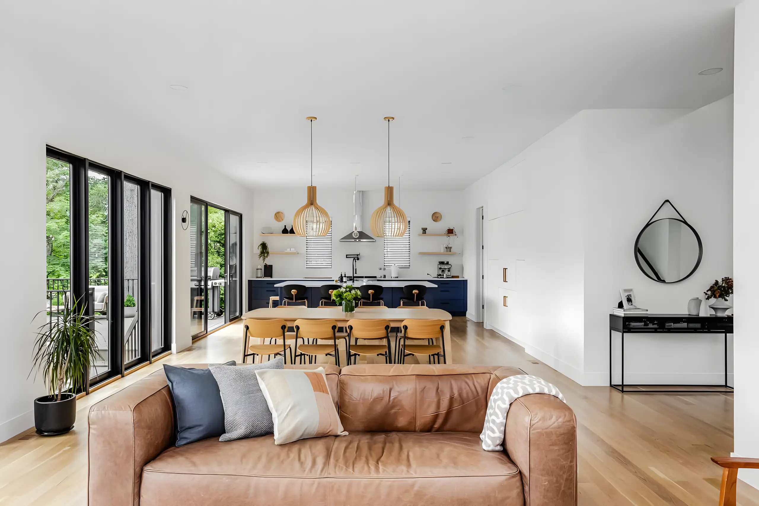 Dining table under brass pendants with the kitchen beyond and a round mirror