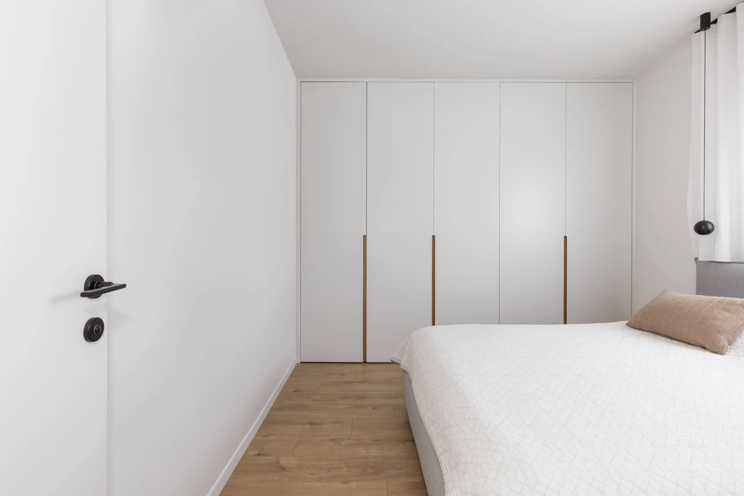 White wardrobe doors with brass handles beside a bed