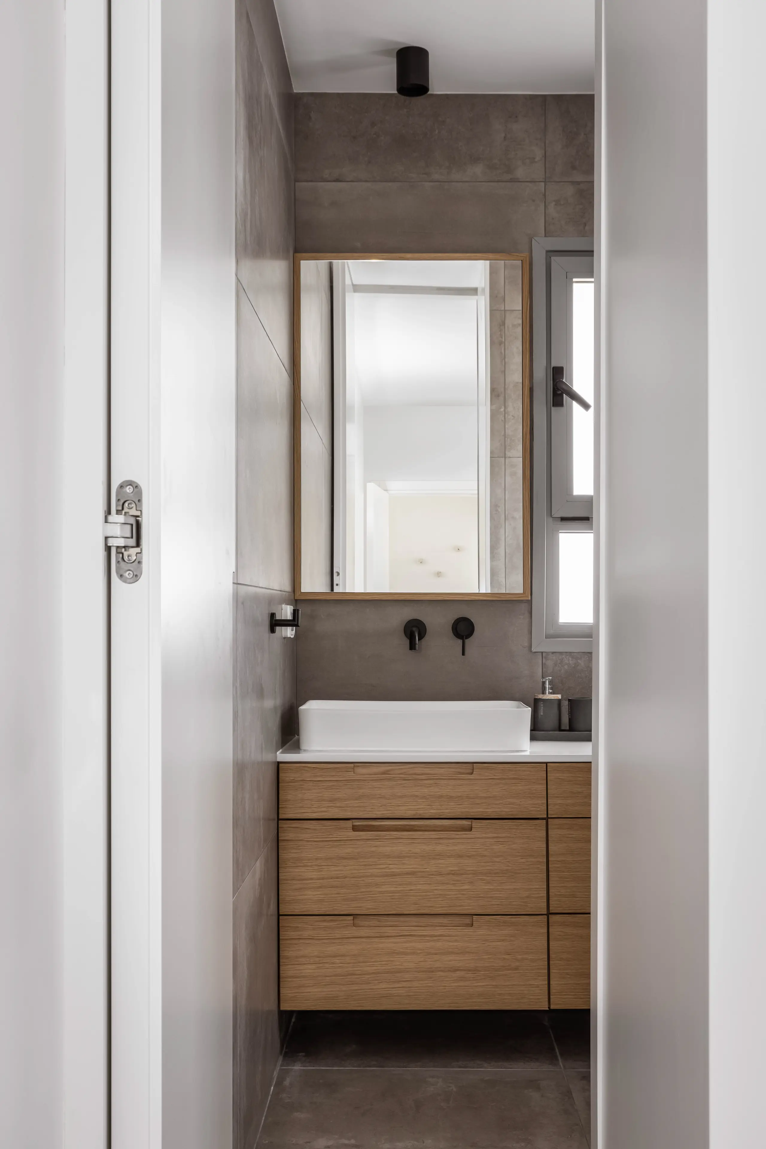 Bathroom in grey tile with an oak vanity and a black tap