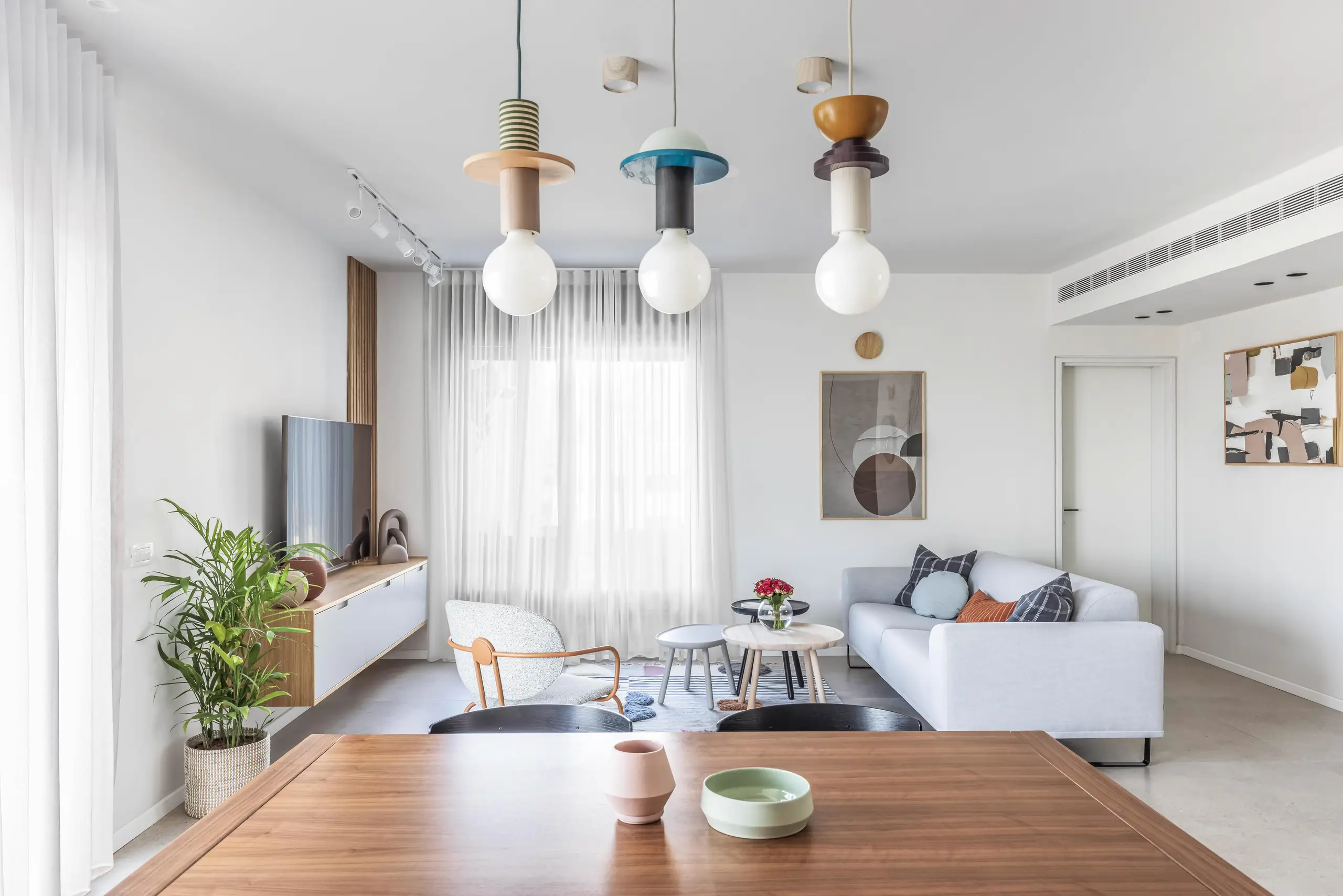 Dining table under three coloured pendants with the kitchen beyond