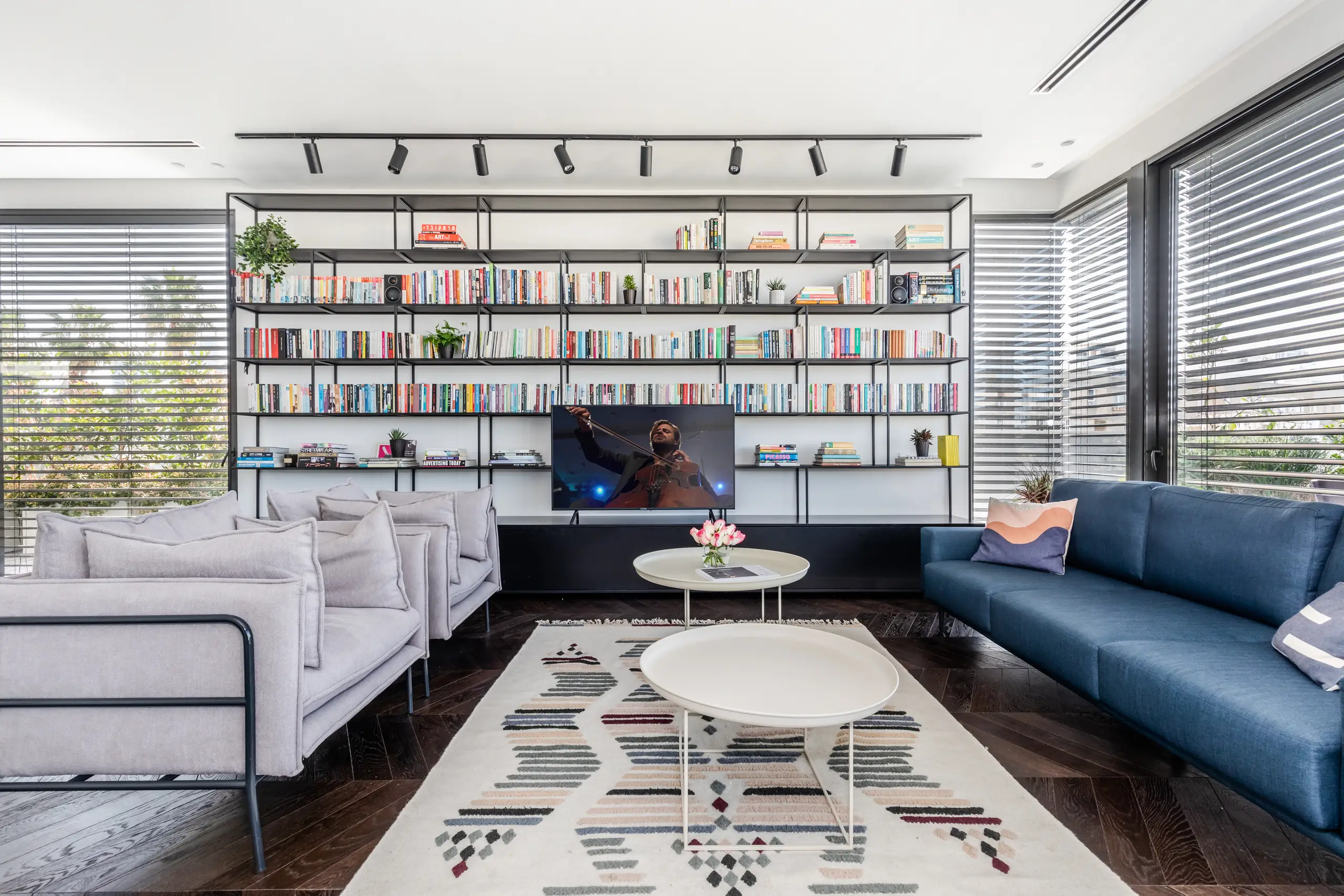 Living room with a blue sofa, a full wall of open shelving and a patterned rug