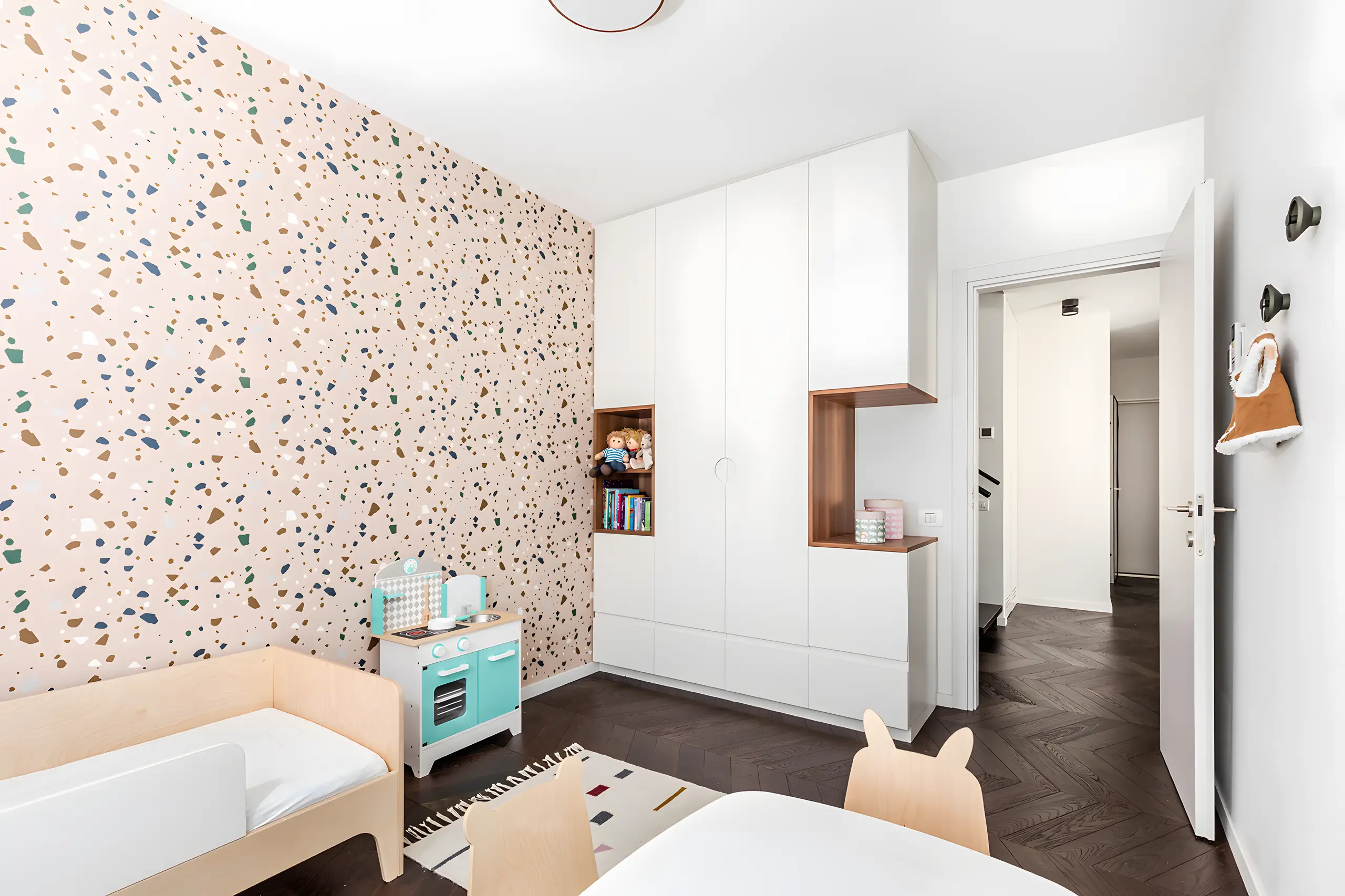 Child's room with terrazzo-patterned wallpaper and white joinery