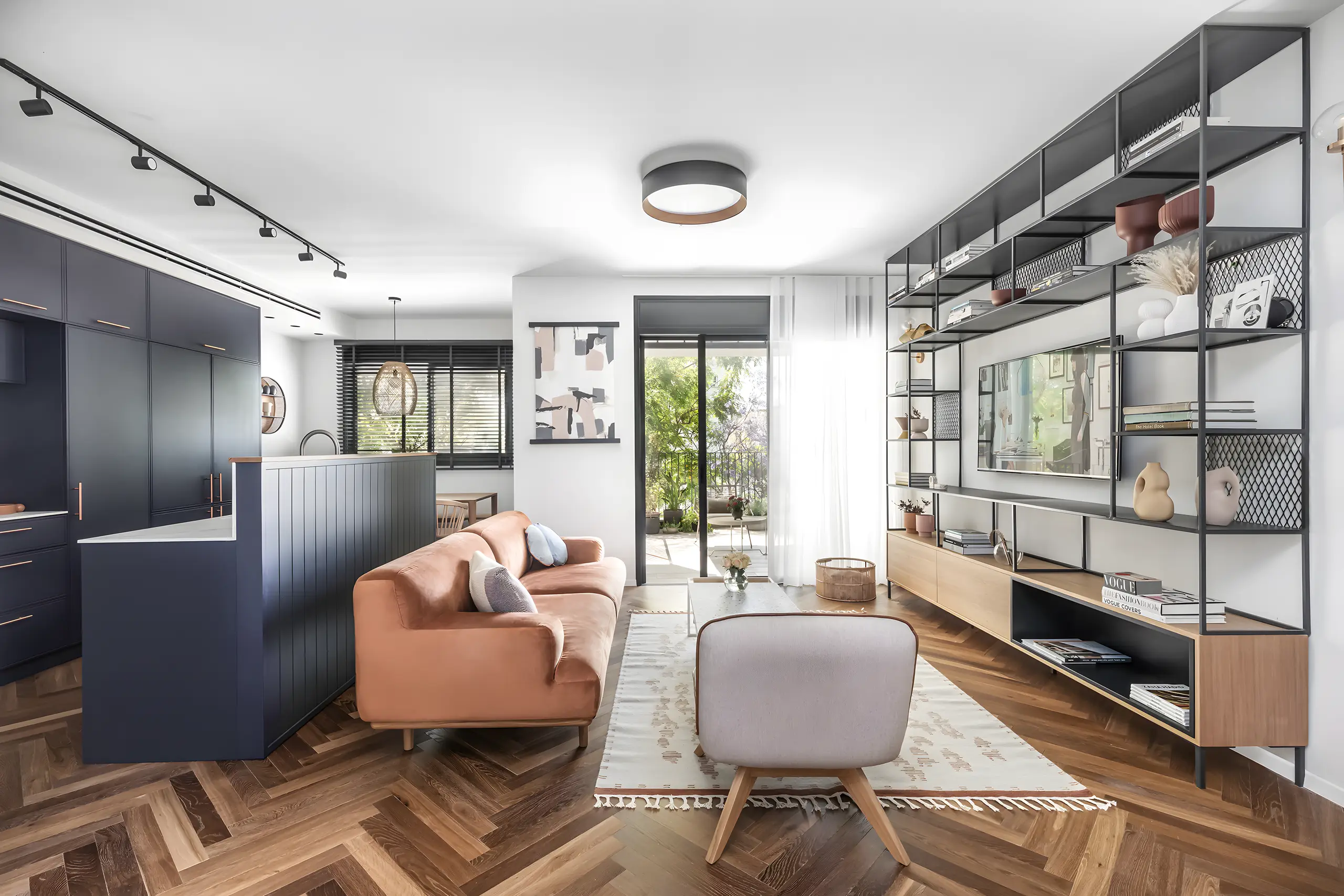 Navy kitchen block, open steel bookcase and an orange sofa on herringbone oak