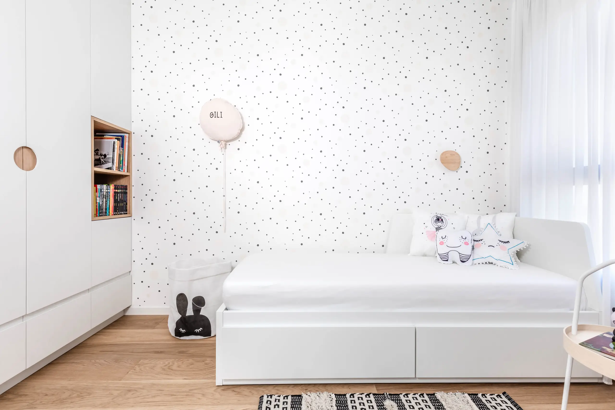Built-in bed under a wall of dark-grey wallpaper with a white bookshelf niche