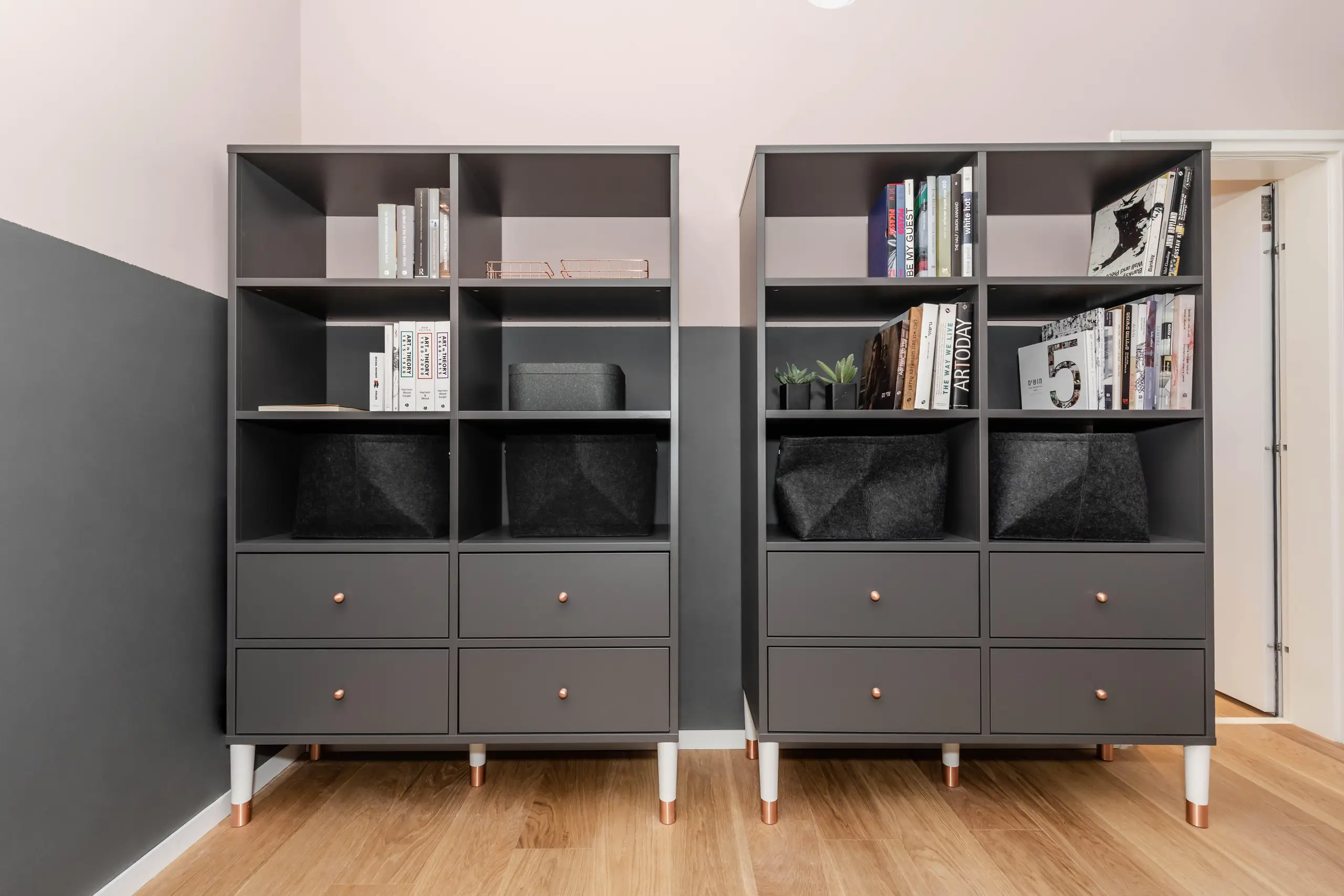 Two grey bookcases with drawers against a white wall