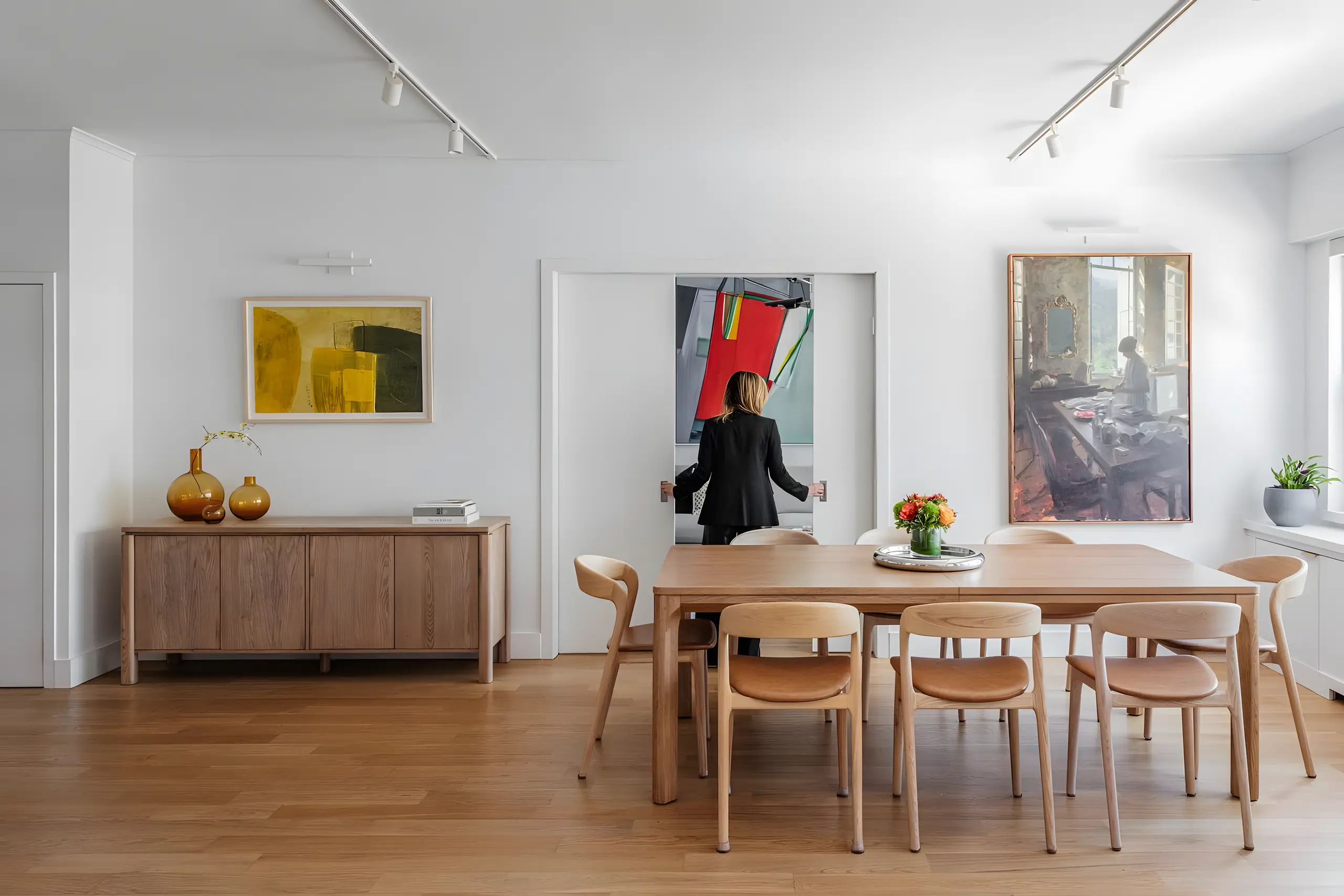 Dining table and chairs in pale oak beside pocket doors, art on every wall